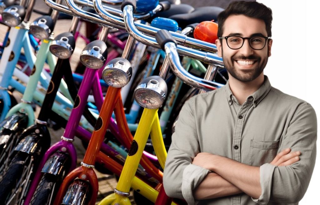 homme souriant bras croisés et derrière lui il y à de nombreux vélo coloré aligné