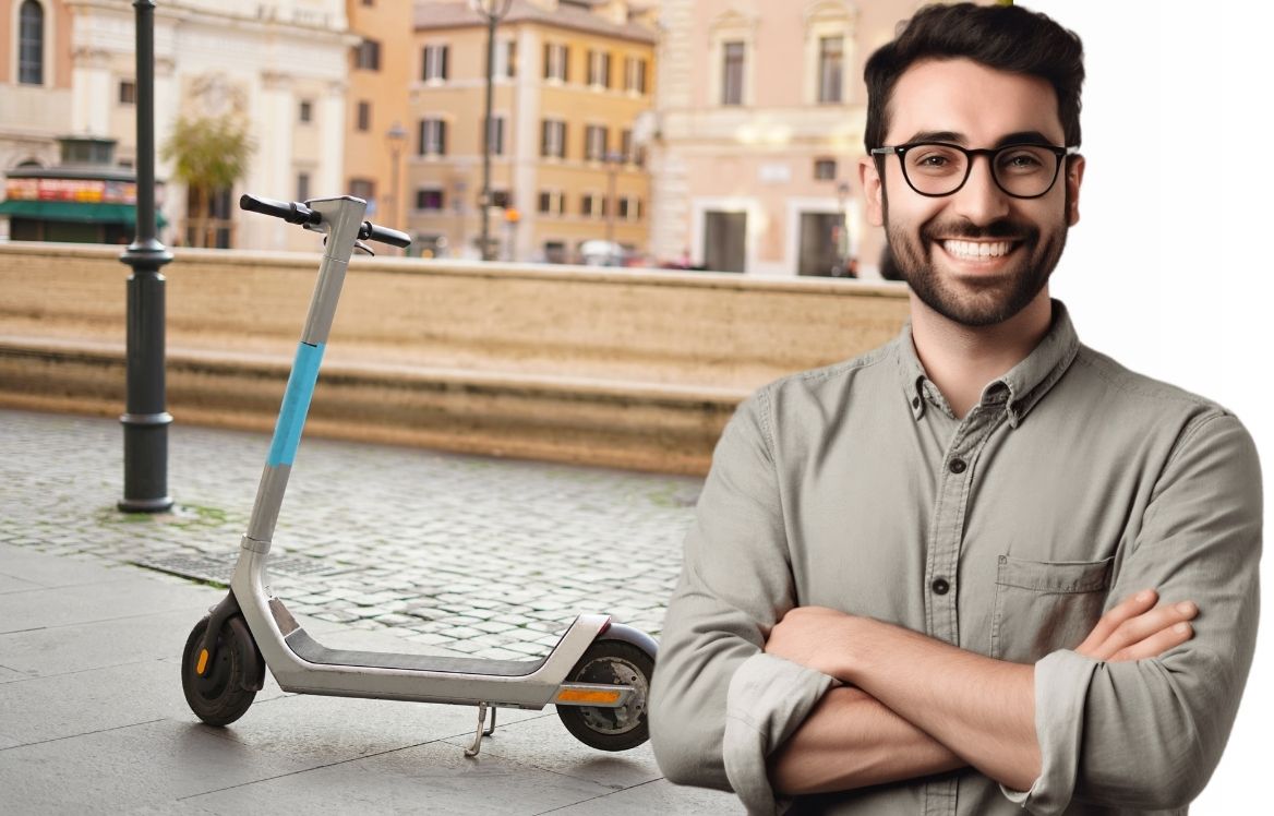 homme souriant bras croisée et derrière lui une trottinette électrique dans la rue