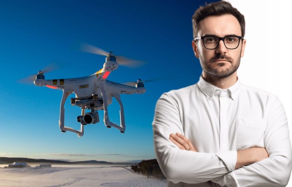 homme bras croisée qui vous regarde et en arrière plan il y à une photo d'un drone dans le ciel