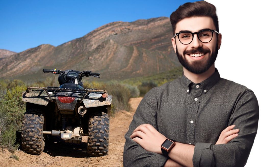 homme souriant les bras croisés, et en arrière plan il y a un quad dans le désert