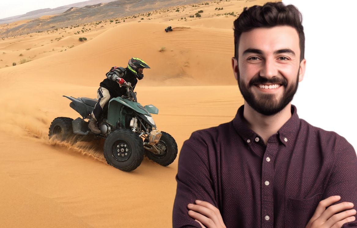 Homme souriant, bras croisés. en arrière plan il y à un homme sur un quad dans le désert qui roule