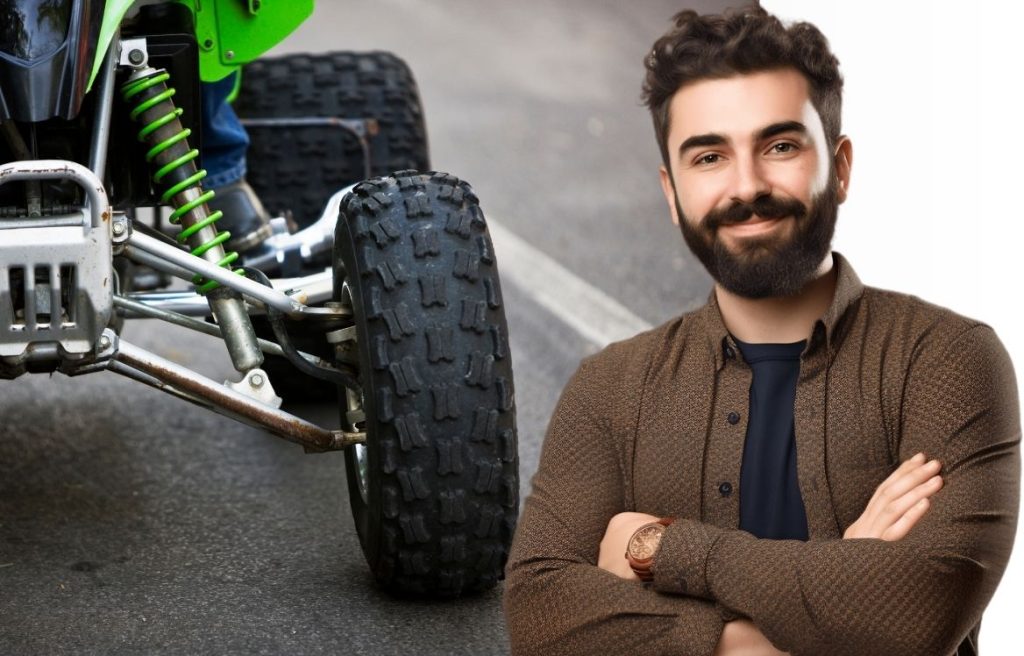 homme souriant bras croisés, derrière lui il y a un quad en gros plan.