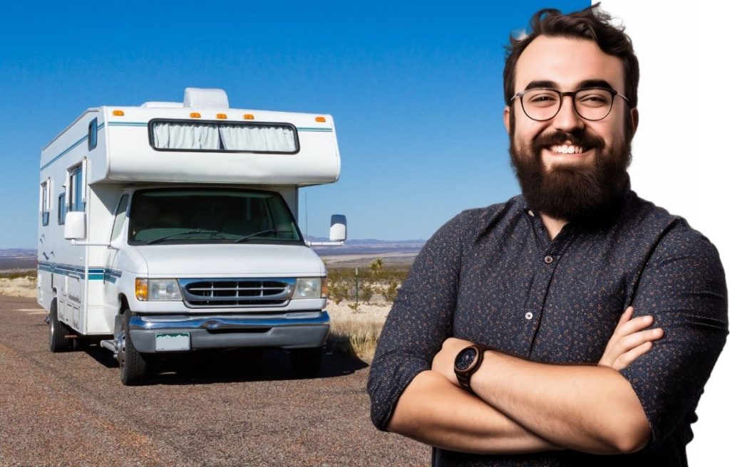 homme souriant bras croisés et derrière lui il y a un camping car vu de face sur une route