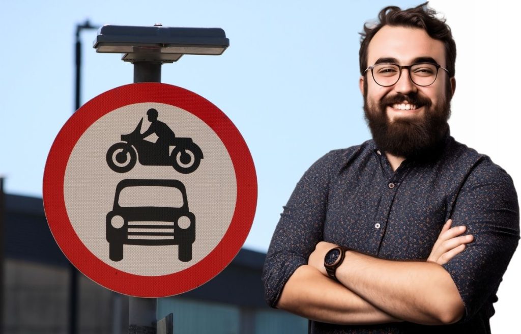 homme souriant les bras croisés au premier plan et derrière lui, il y a un panneau qui montre une moto et une voiture.