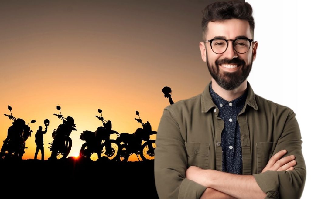 homme souriant au premier plan et derrière lui il y a un paysage avec des moto aligné devant un couché de soleil