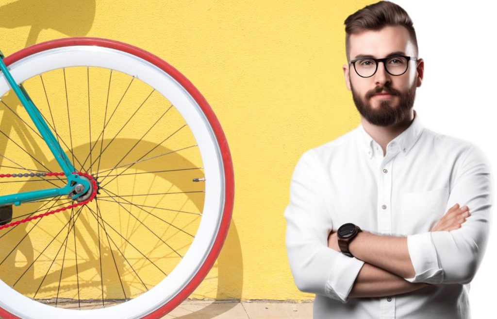 homme souriant bras croisée et derrière lui il ya un mur jaune et une roue de vélo devant le mur