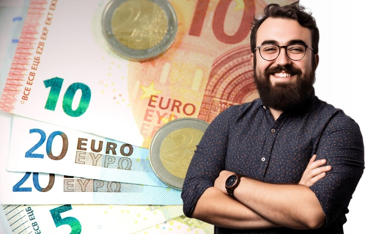 Cette image représente un homme debout et souriant bras croisé qui vous regarde. En fond, vous retrouvez des billets de 10€ et 20€ et des pièces de 2 euros. Cette image représente le titre de l'article "Comprendre le coût de l'assurance de prêt"